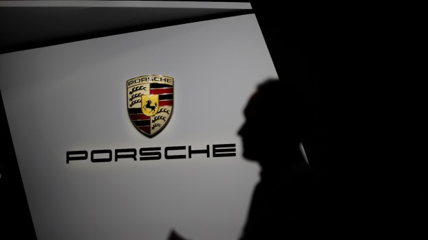 Man stands in front of the Porsche logo at an auto show.