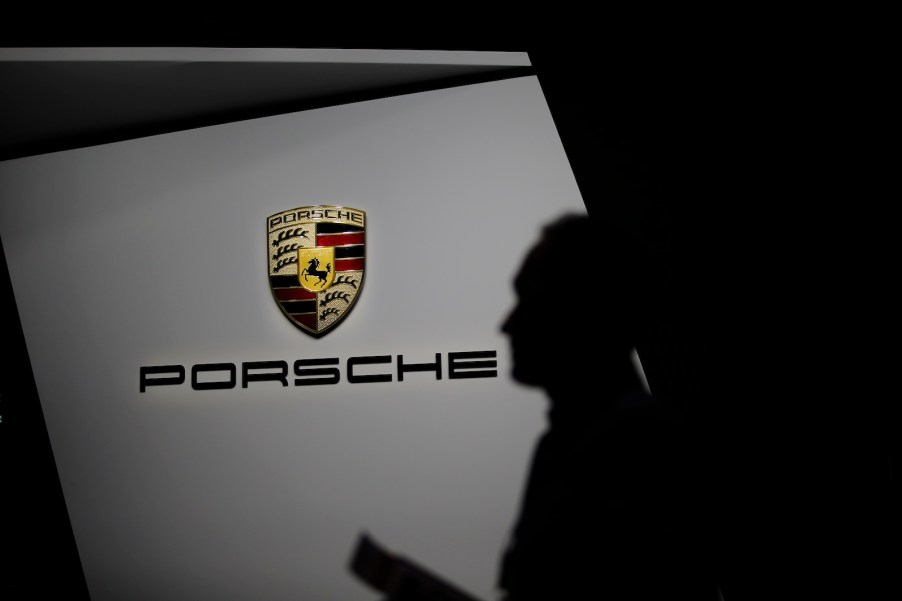 Man stands in front of the Porsche logo at an auto show.
