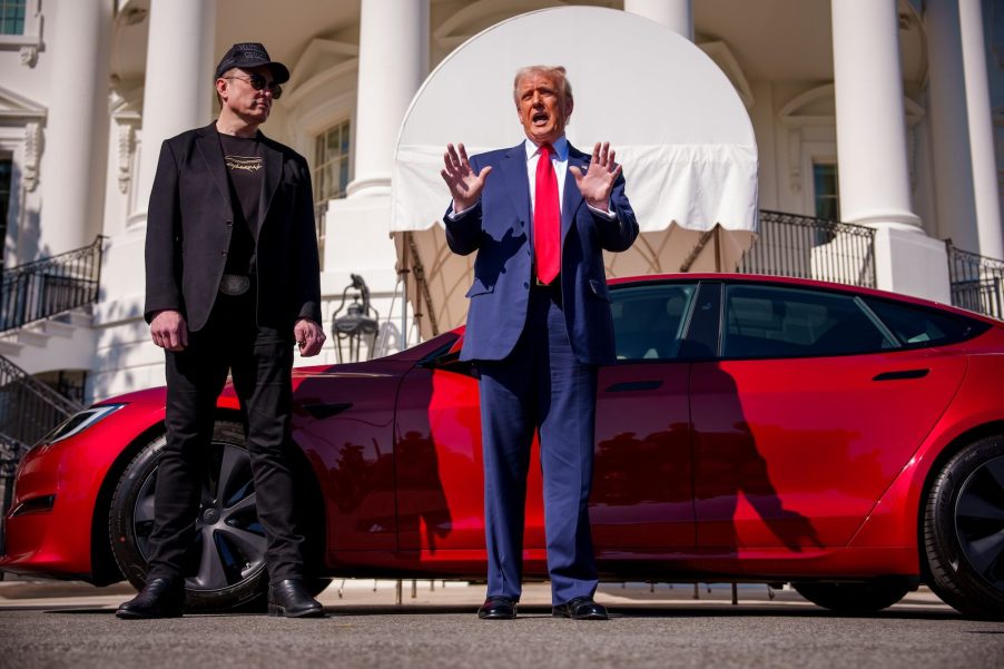 President Donald Trump and Elon Musk stand next to red Tesla outside the White House