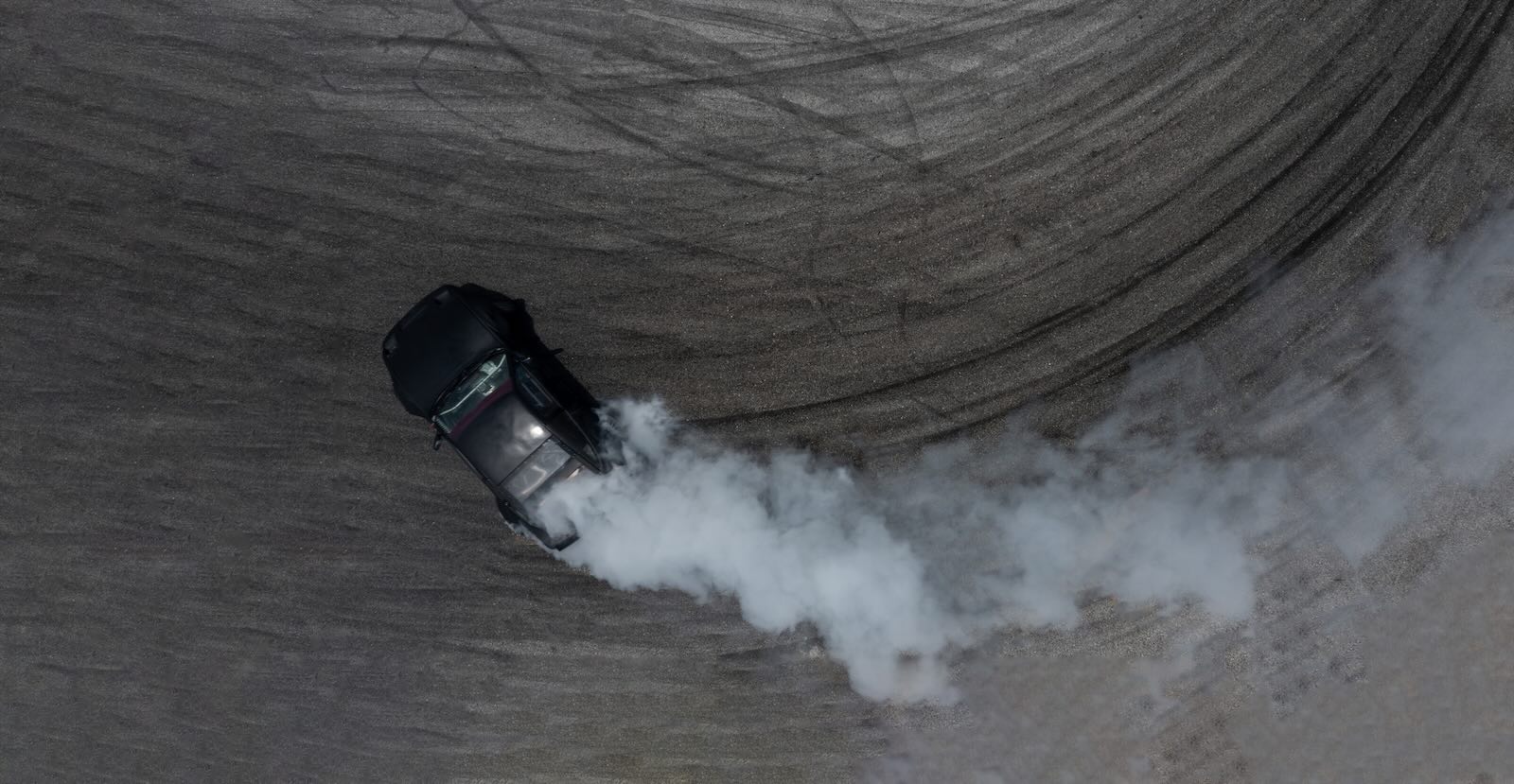 Smoke rising from a black car drifting through a donut while street racing.