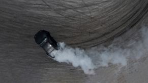 Smoke rising from a black car drifting through a donut while street racing.