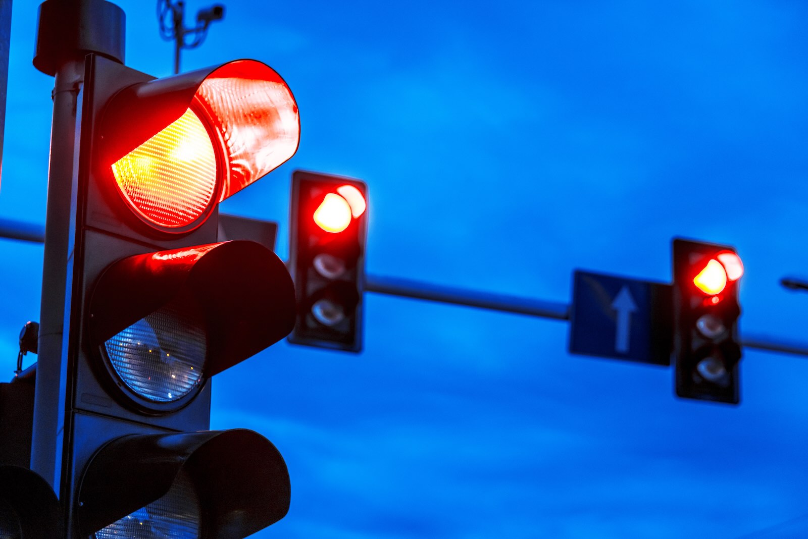 Three red traffic lights against a dark blue night sky.