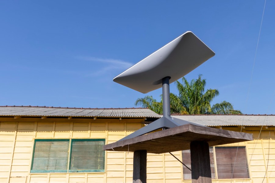 Starlink antenna in front of a house, palm trees in the background.