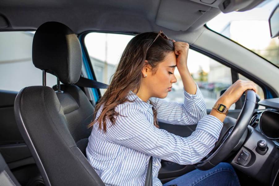 Sad EV driver leans against her Tesla steering wheel, eyes closed.