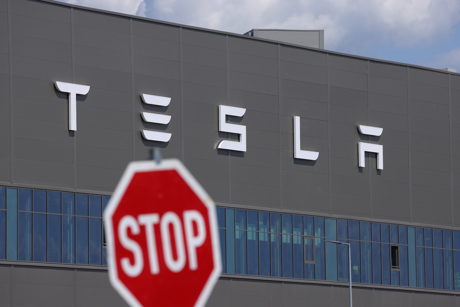 Traffic "stop" sign in front of the Tesla logo on the side of an EV factory.