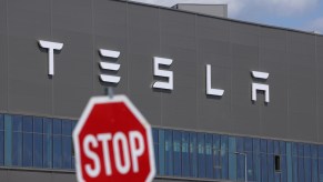 Traffic "stop" sign in front of the Tesla logo on the side of an EV factory.