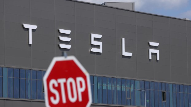 Traffic "stop" sign in front of the Tesla logo on the side of an EV factory.