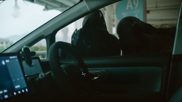 Two men in masks examine car for valuable before breaking in