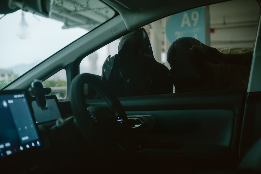 Two men in masks examine car for valuable before breaking in