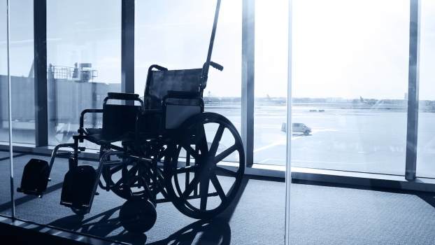 Empty wheelchair parked by window in airport, jet plane parked in the background.