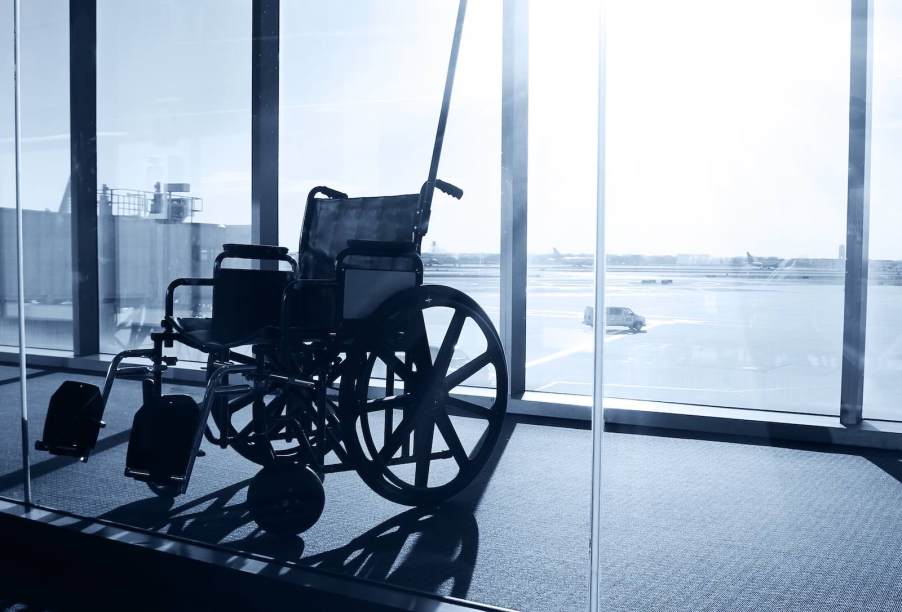Empty wheelchair parked by window in airport, jet plane parked in the background.