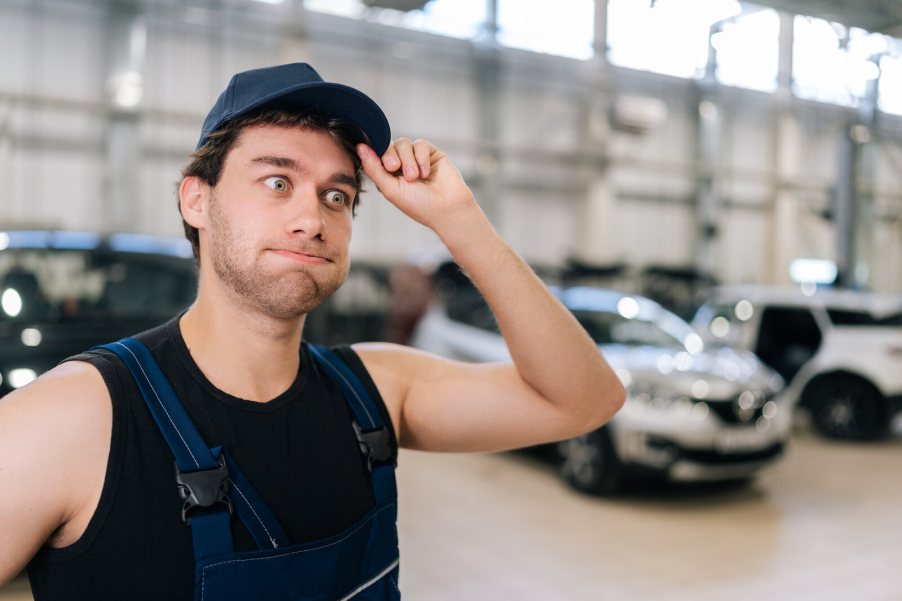 A mechanic holds his hat makes a "oops" face blowing out air