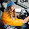 A female driver in winter coat and hat turns car heat on holds hand up to dash vent