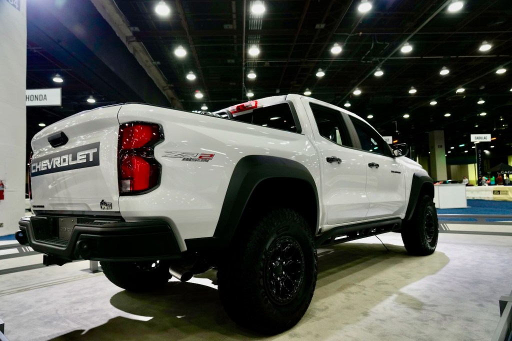 The bed and rear tire of a white Chevrolet Colorado midsize pickup truck parked at an auto show.