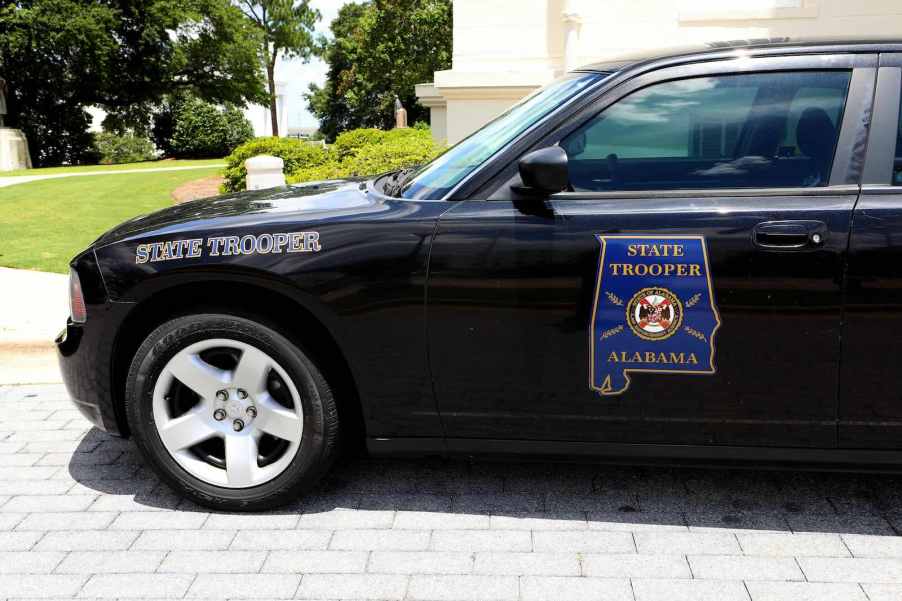 Black Dodge Charger patrol car with an Alabama State Trooper door badge parked by a park.