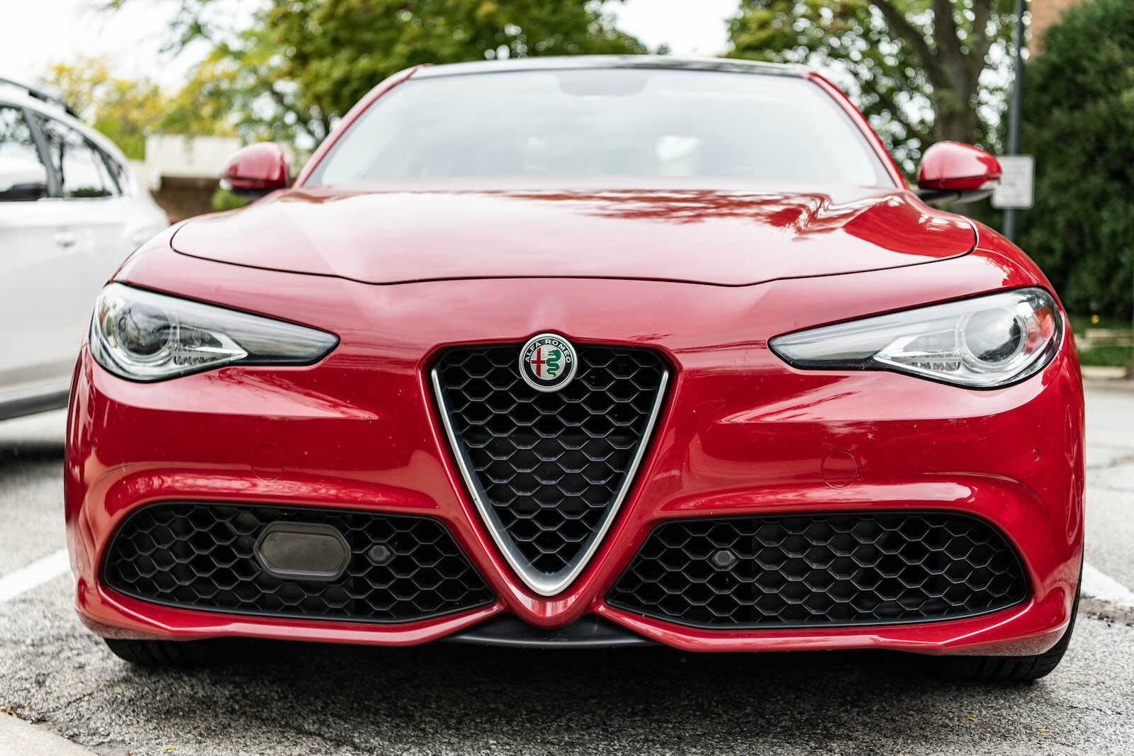 Front of a red Alfa Romeo Giulia sedan, a parking lot visible in the background.