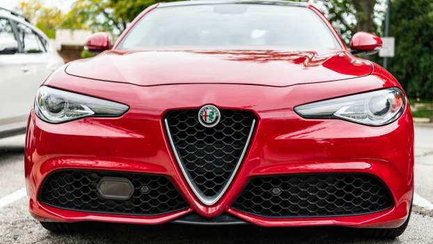 Front of a red Alfa Romeo Giulia sedan, a parking lot visible in the background.