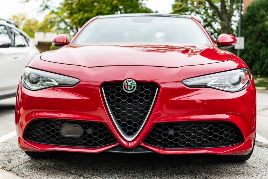 Front of a red Alfa Romeo Giulia sedan, a parking lot visible in the background.