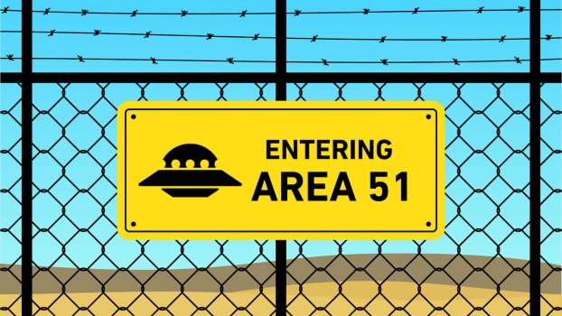 Bright yellow Area 51 cartoon sign on a chain link fence with a UFO graphic