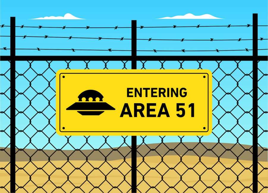 Bright yellow Area 51 cartoon sign on a chain link fence with a UFO graphic