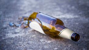 Broken brown beer bottle laying on the pavement of a road.