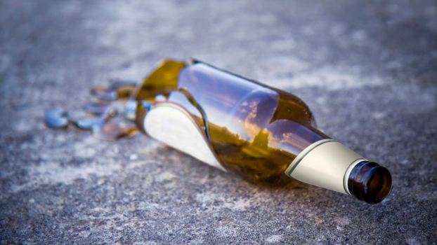 Broken brown beer bottle laying on the pavement of a road.