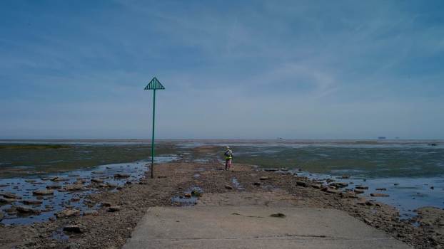 A hiker sets out on beach mudflats, the ocean visible beyond.
