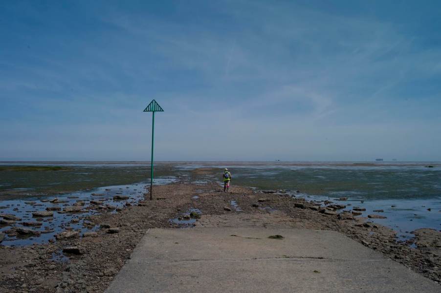 A hiker sets out on beach mudflats, the ocean visible beyond.