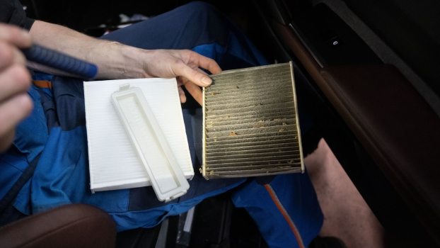 Technician holds an old and new cabin air filter in a car