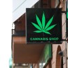 Cannabis Shop sign with a marijuana leaf hangs above a dispensary door.