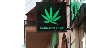 Cannabis Shop sign with a marijuana leaf hangs above a dispensary door.