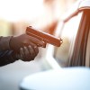 A man stealing a car with a gun