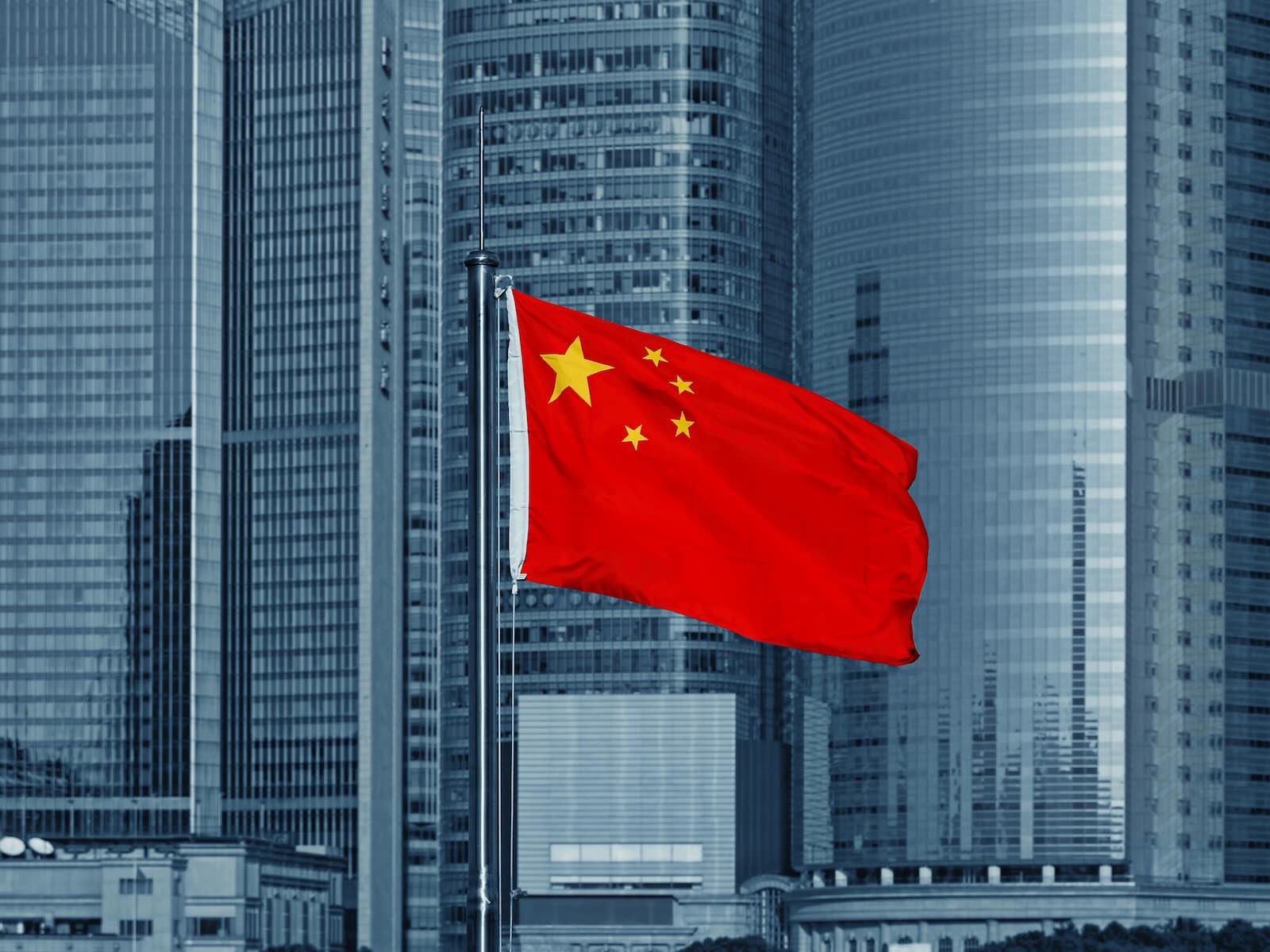 Red Chinese flag in front of skyscrapers.
