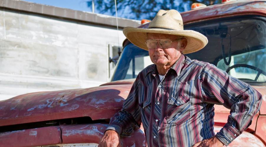 Older pickup truck driver leans against his Silverado hood.