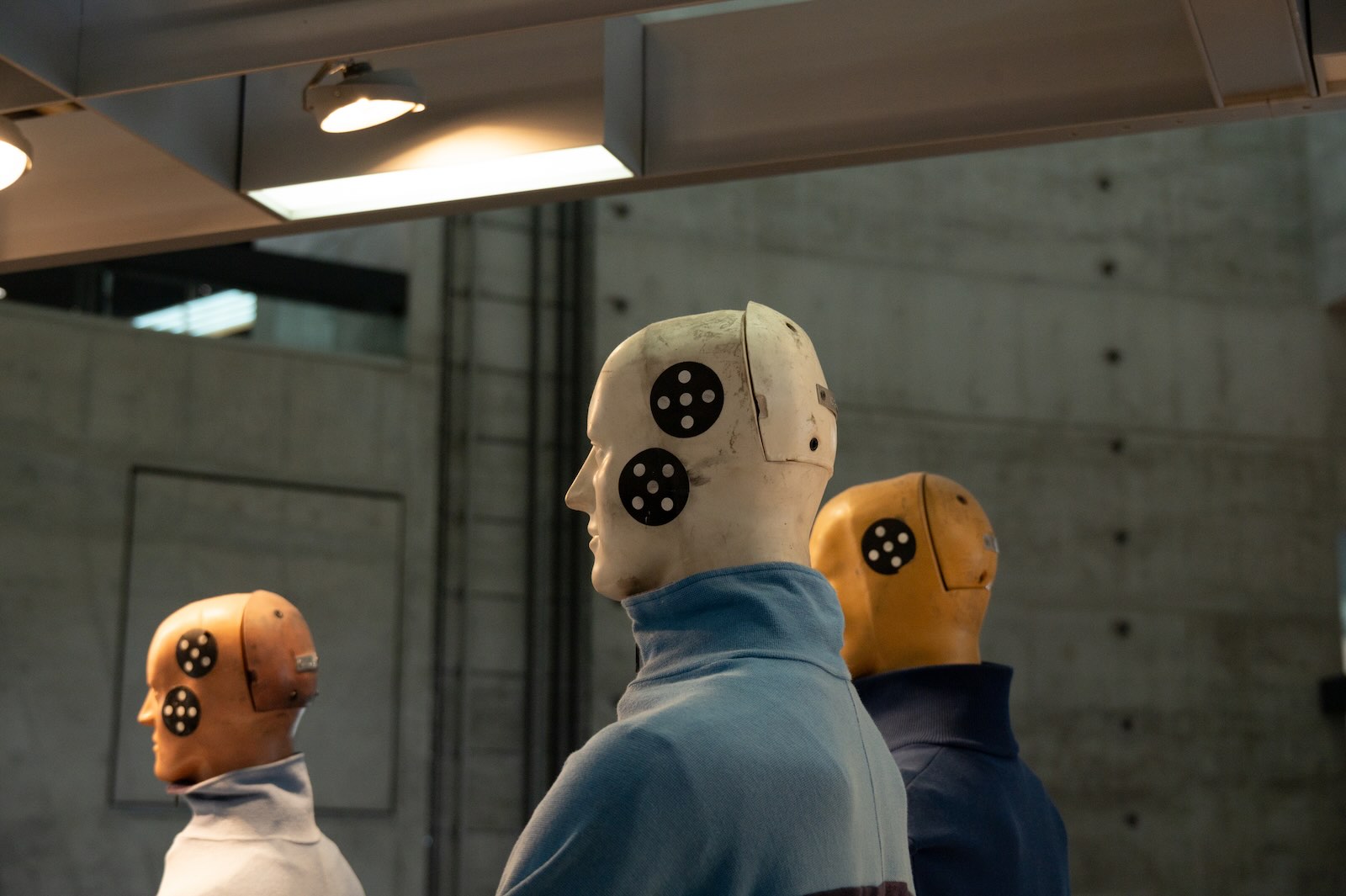 Three crash test dummies used for automotive safety ratings, with a concrete wall in the background.