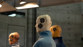 Three crash test dummies used for automotive safety ratings, with a concrete wall in the background.