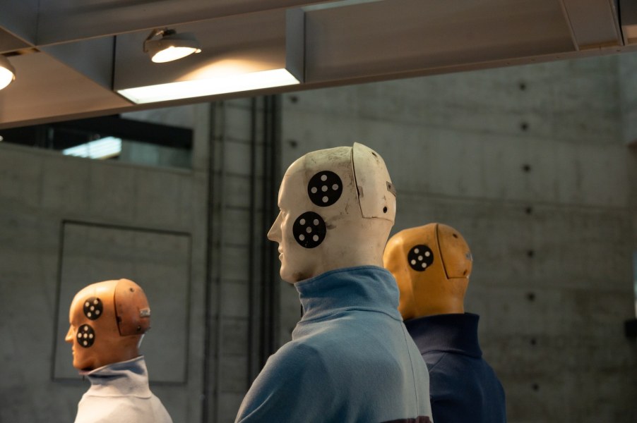 Three crash test dummies used for automotive safety ratings, with a concrete wall in the background.