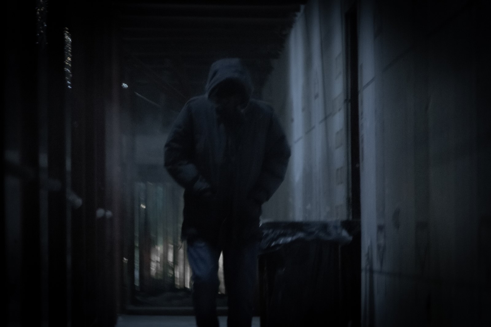 Man with a hood over his face walks through a dark alleyway