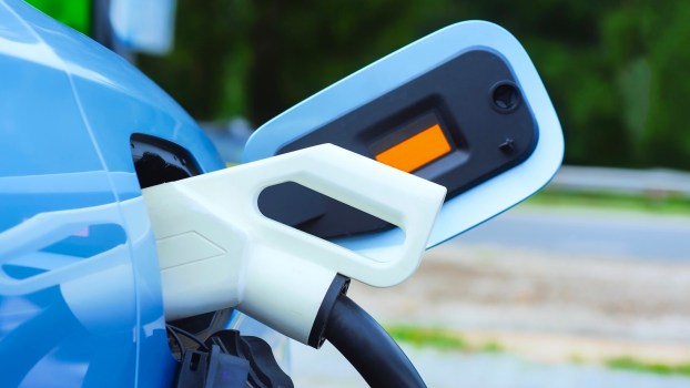 Blue electric vehicle hooked up to a charging cable.