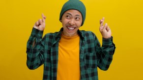 Mini Cooper driver smiles and crosses their fingers, in front of a yellow backdrop.