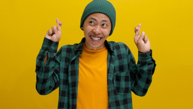 Mini Cooper driver smiles and crosses their fingers, in front of a yellow backdrop.