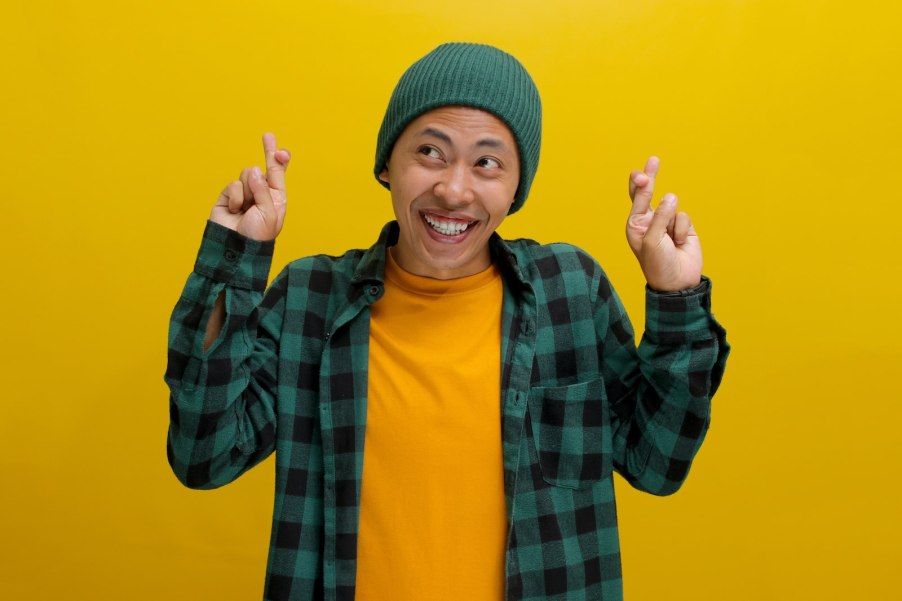 Mini Cooper driver smiles and crosses their fingers, in front of a yellow backdrop.