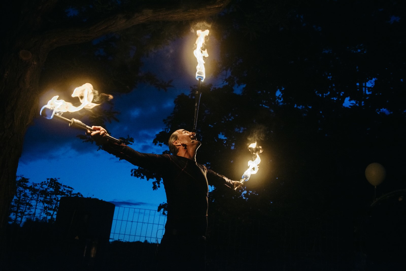 Man holds up three flaming juggling clubs, a dark sky visible in the background.