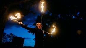 Man holds up three flaming juggling clubs, a dark sky visible in the background.