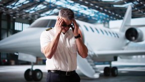 Frustrated pilot standing in front of a small jet with his head in his hands.
