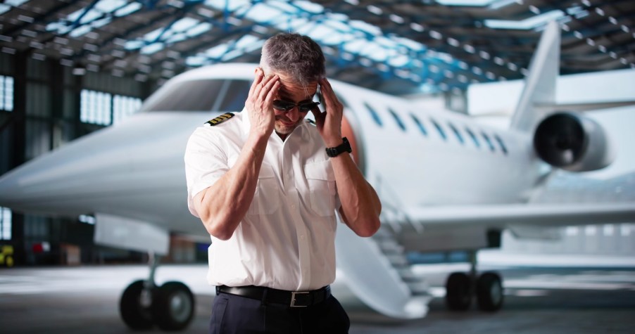 Frustrated pilot standing in front of a small jet with his head in his hands.