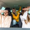 Three young women make silly faces while sitting in a car.