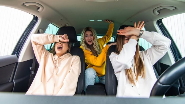 Three young women make silly faces while sitting in a car.