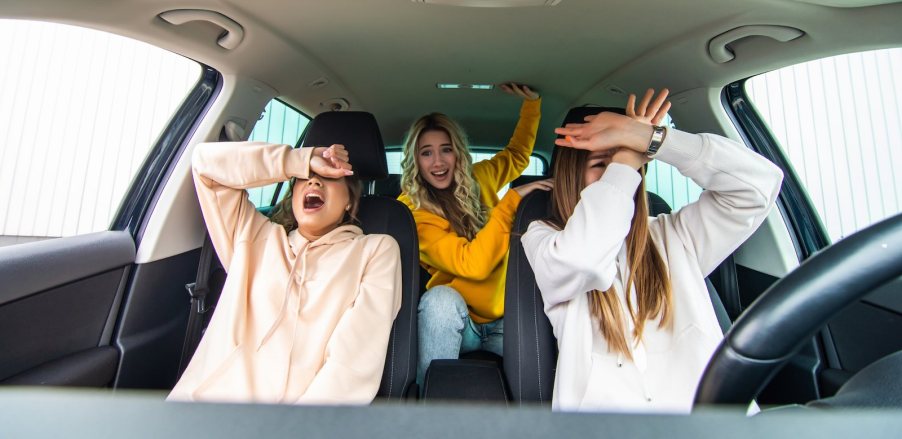 Three young women make silly faces while sitting in a car.