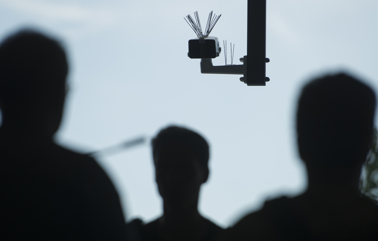 The silhouettes of a crowd of people approach a surveillance camera.